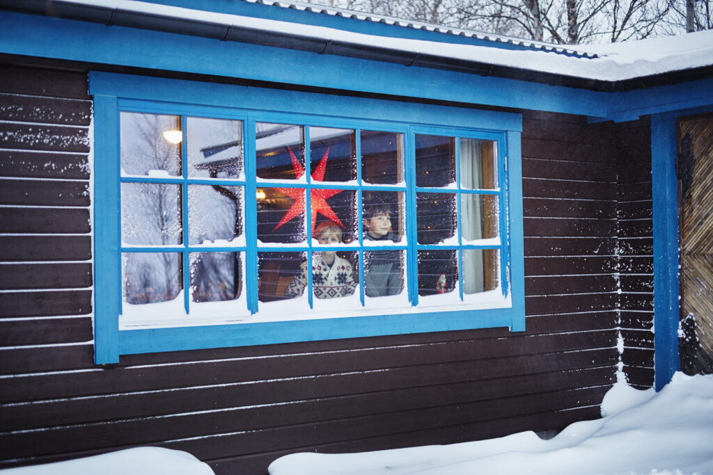 Two brothers looking out of a snow-covered cabin window, highlighting the benefits of replacing windows in winter for improved energy efficiency and comfort during colder months.