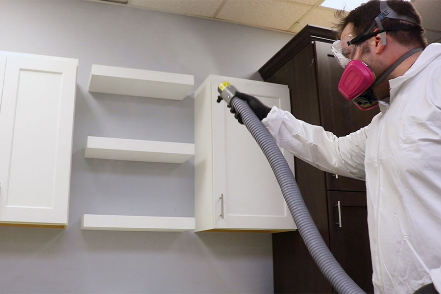 Professional wearing a respirator and protective gear applying commercial office disinfection services with a precision spray nozzle to shelves and cabinetry