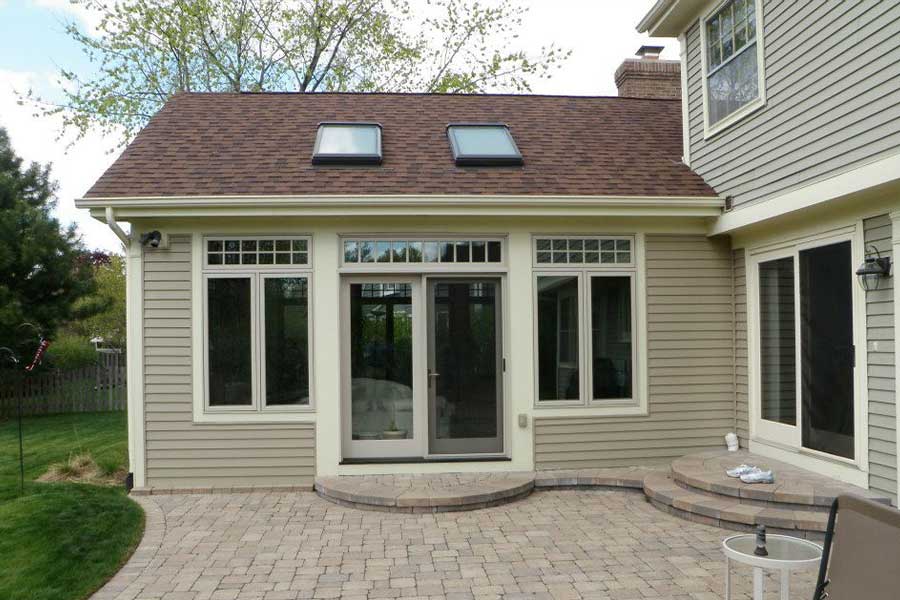 Efficient window replacement services displayed on a home with beige siding, French doors, and a brown shingle roof with skylights