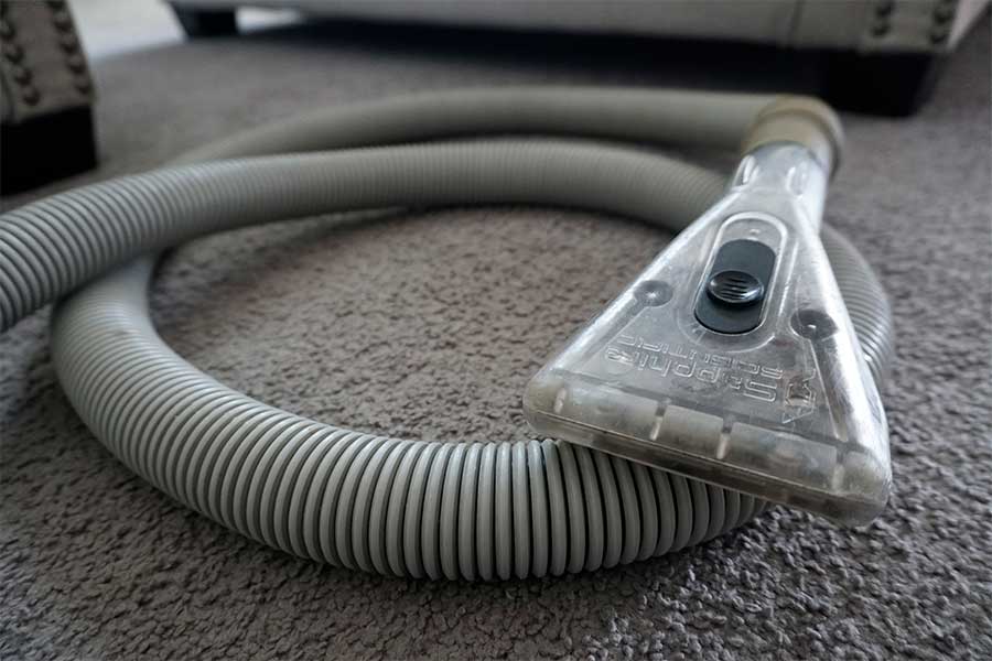 Close-up of a professional upholstery cleaning service's equipment, featuring a transparent vacuum head on a textured carpet, ready for deep cleaning