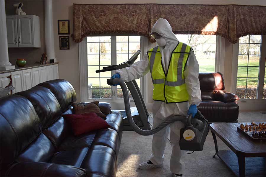 Expert in protective suit from the best commercial disinfection services using high-tech fogging equipment to sterilize a home office with leather furniture and elegant decor