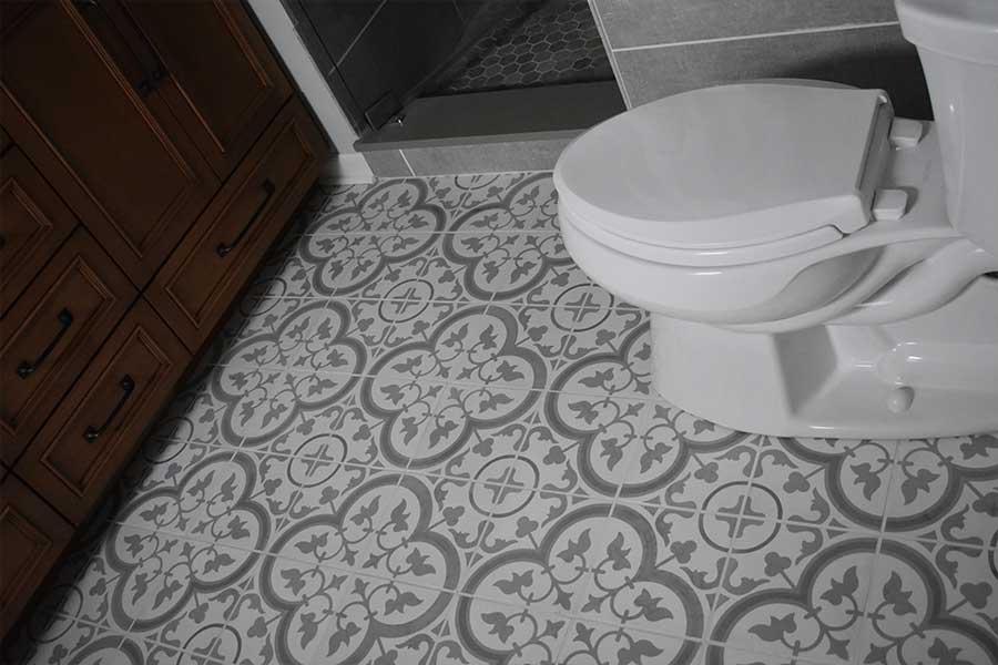 Detail of a bathroom floor after a grout and tile cleaning service, highlighting the intricate gray and white tiles and the wooden vanity's craftsmanship