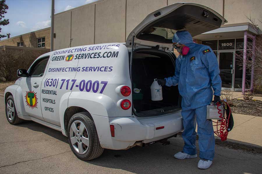 Professional in protective gear preparing commercial disinfection services equipment from a branded vehicle, ready to sanitize a facility