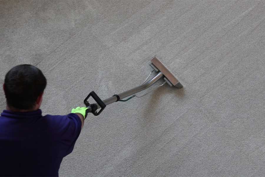 Overhead view of a professional carpet cleaning services technician using an industrial-grade steam wand to deep clean a textured beige carpet