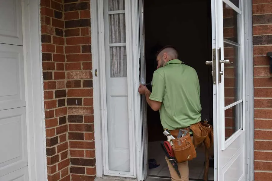 Professional installer concentrating on a door replacement service, securing a new door in a brick home entryway, equipped with all necessary tools