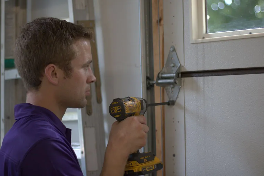 Focused technician from a local garage door repair service using a power drill to adjust hardware, ensuring the door operates smoothly and safely