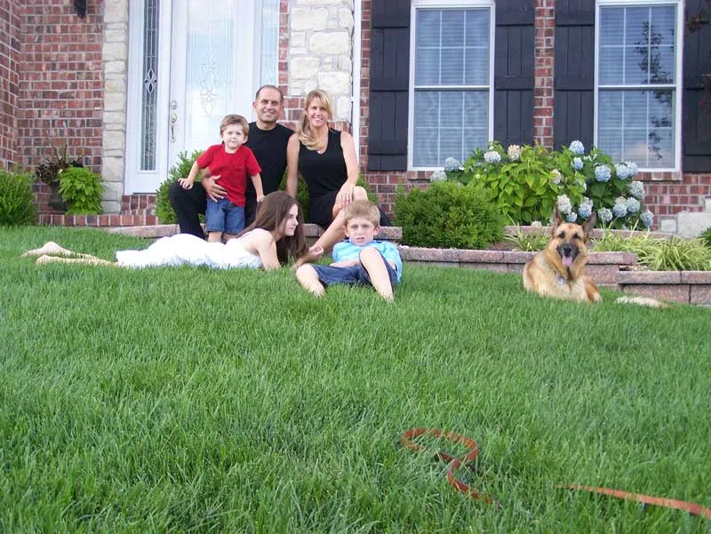 A happy family and their dog relaxing on lush grass in front of their home, showcasing the beauty of a lawn maintained by local lawn care services