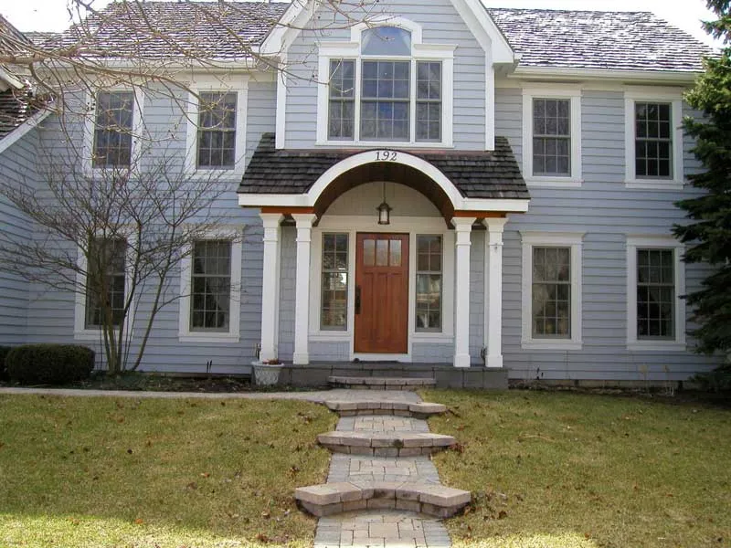 Traditional two-story home with a fresh update from siding replacement services, featuring a classic wooden door, stone path, and white-trimmed windows for curb appeal