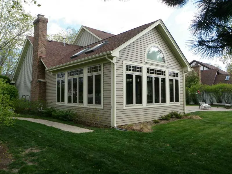 A home addition with multiple windows, including a half-round feature window, highlights the craftsmanship of home window replacement services, set against beige siding and a green lawn