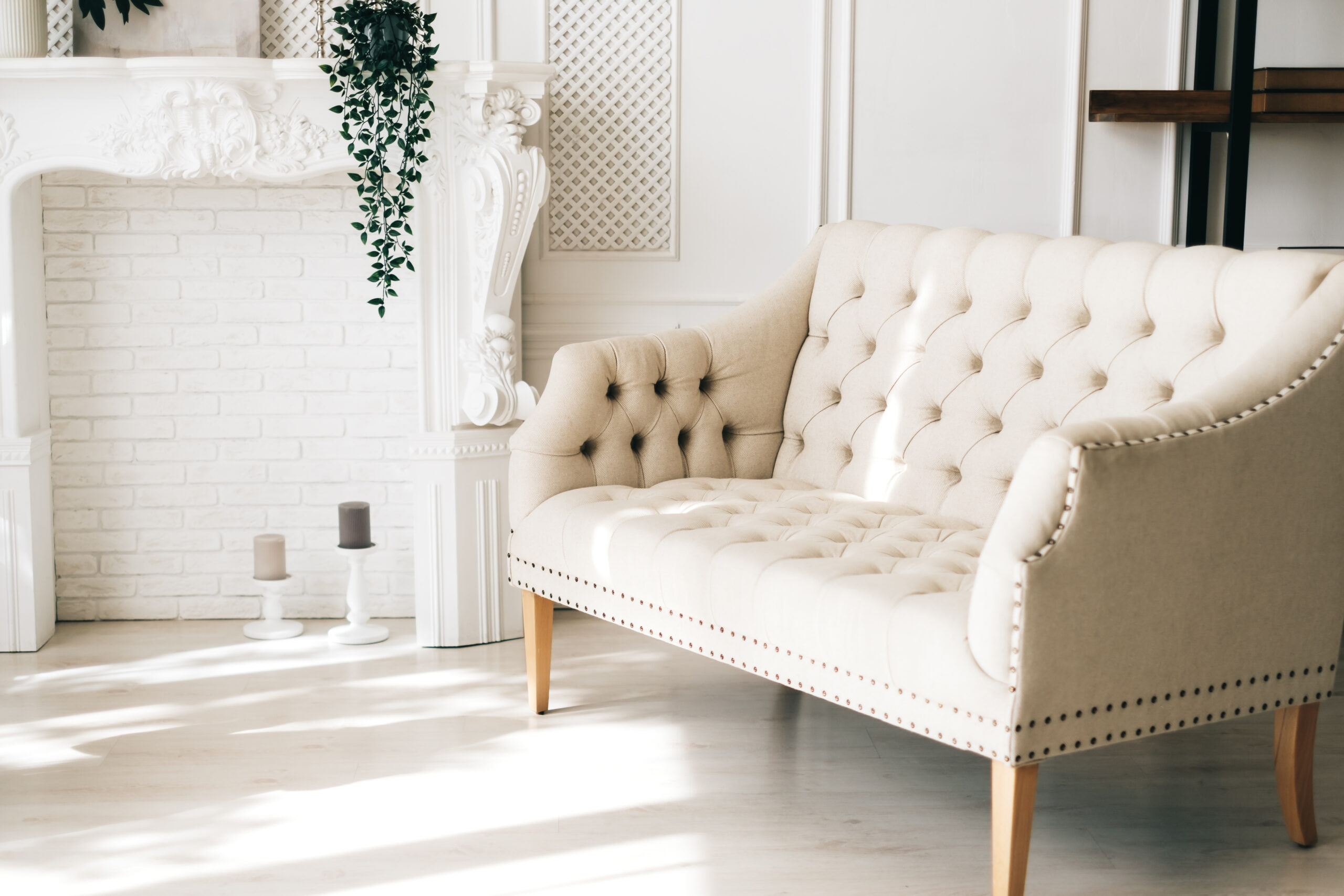 A beige tufted sofa in a bright, elegant living room with a white brick fireplace, showcasing the importance of upholstery cleaning for maintaining furniture. This image highlights key tips for effective upholstery cleaning, especially for lighter fabrics.
