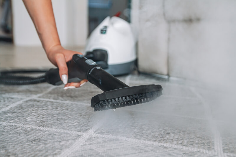 Close-up of a person using a steam cleaner on a tiled floor, illustrating a professional tile and grout cleaning technique, which is important when considering how much grout cleaning costs.