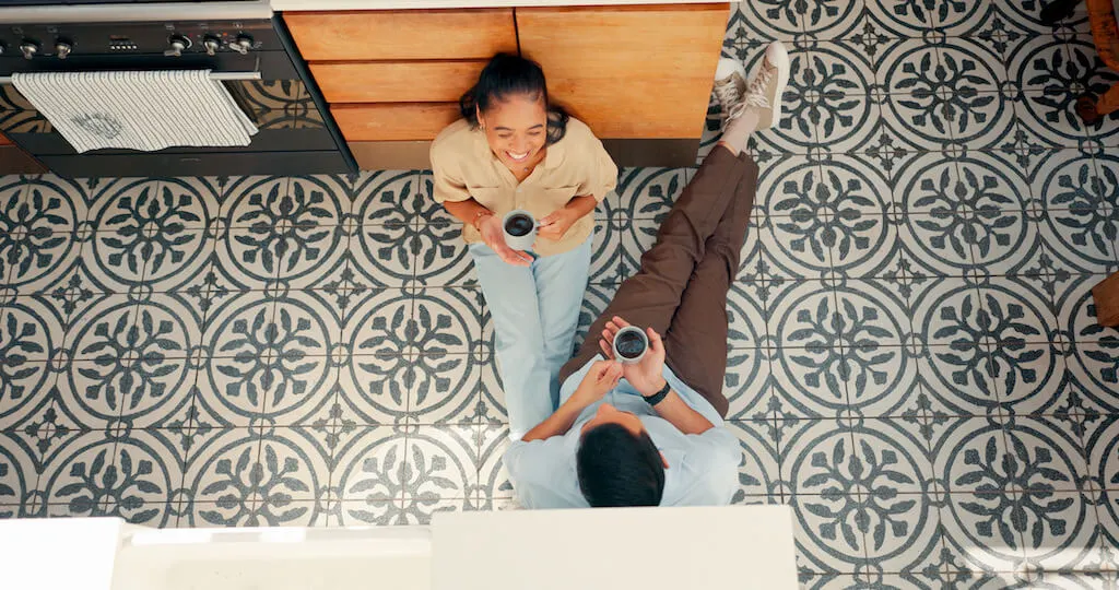 A couple enjoys coffee while sitting on a beautifully restored patterned tile floor in their kitchen, showcasing the results of tile restoration and tile and grout services