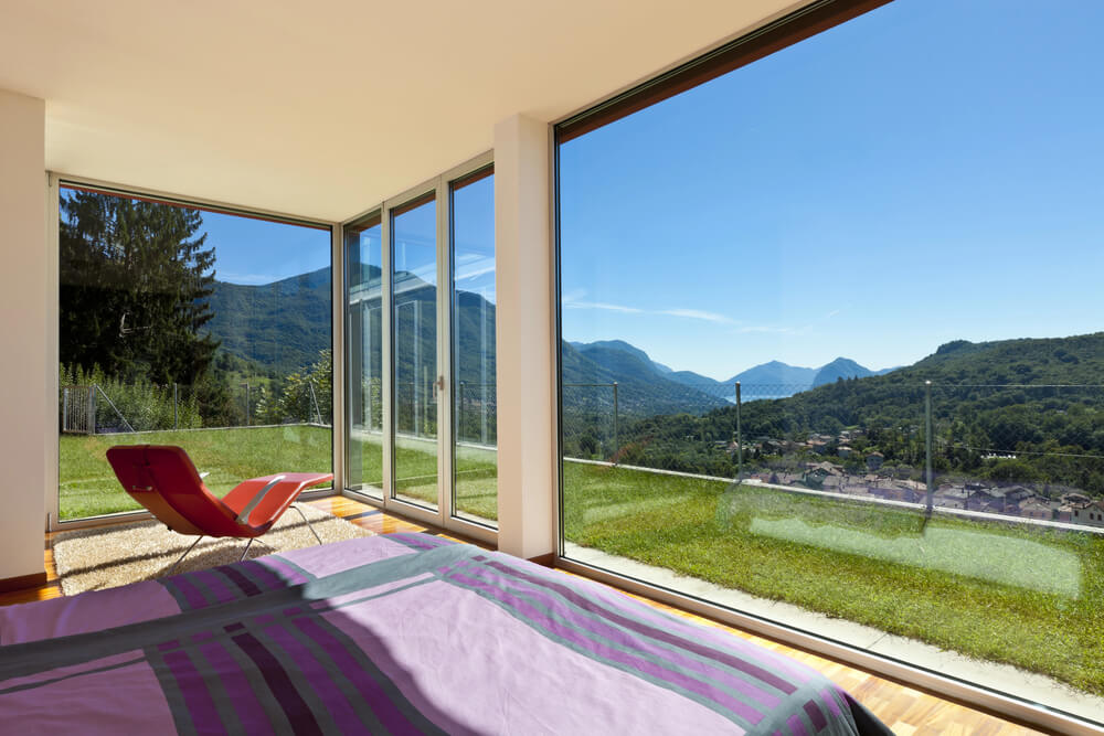 Bedroom with floor-to-ceiling windows offering a stunning mountain view, showing how glass siding can be used creatively among different kinds of siding.