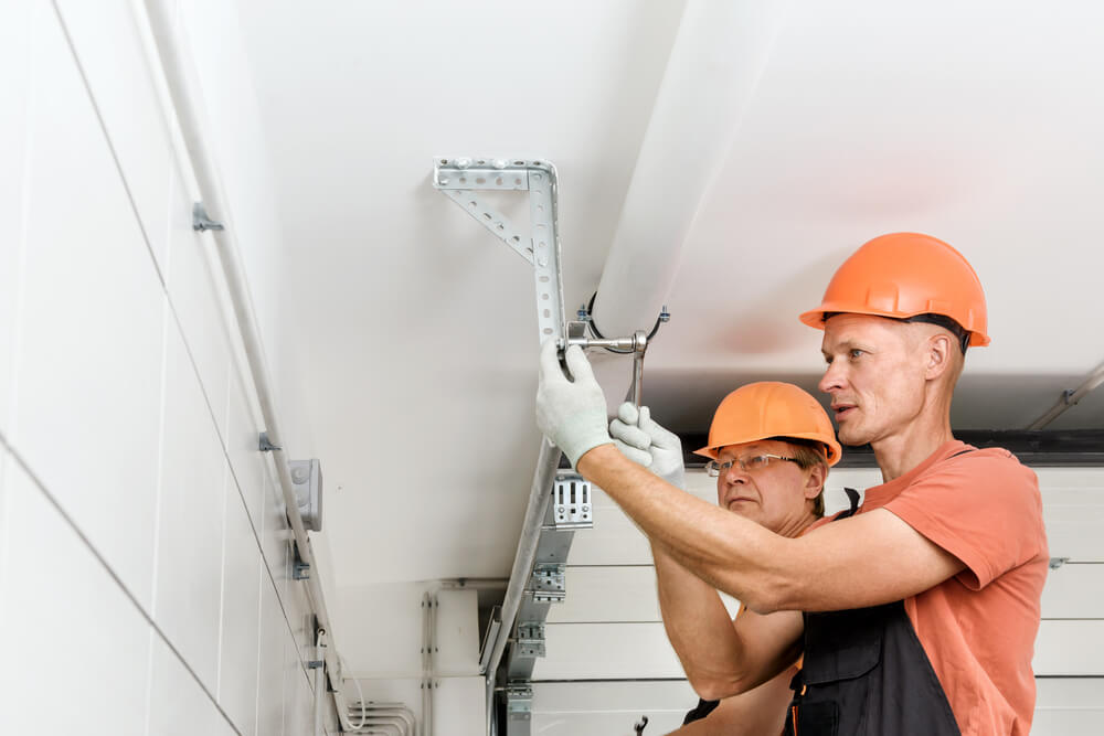 Two workers in hard hats fixing a garage door lift mechanism. A faulty lift mechanism can result in common garage door problems such as misalignment and malfunction.