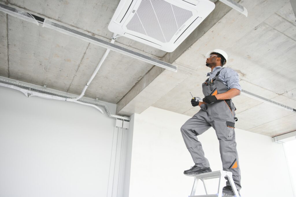 A happy male technician repairing an air conditioner with tools, highlighting the importance of HVAC maintenance and prompting questions like what is the average cost of air duct cleaning 
