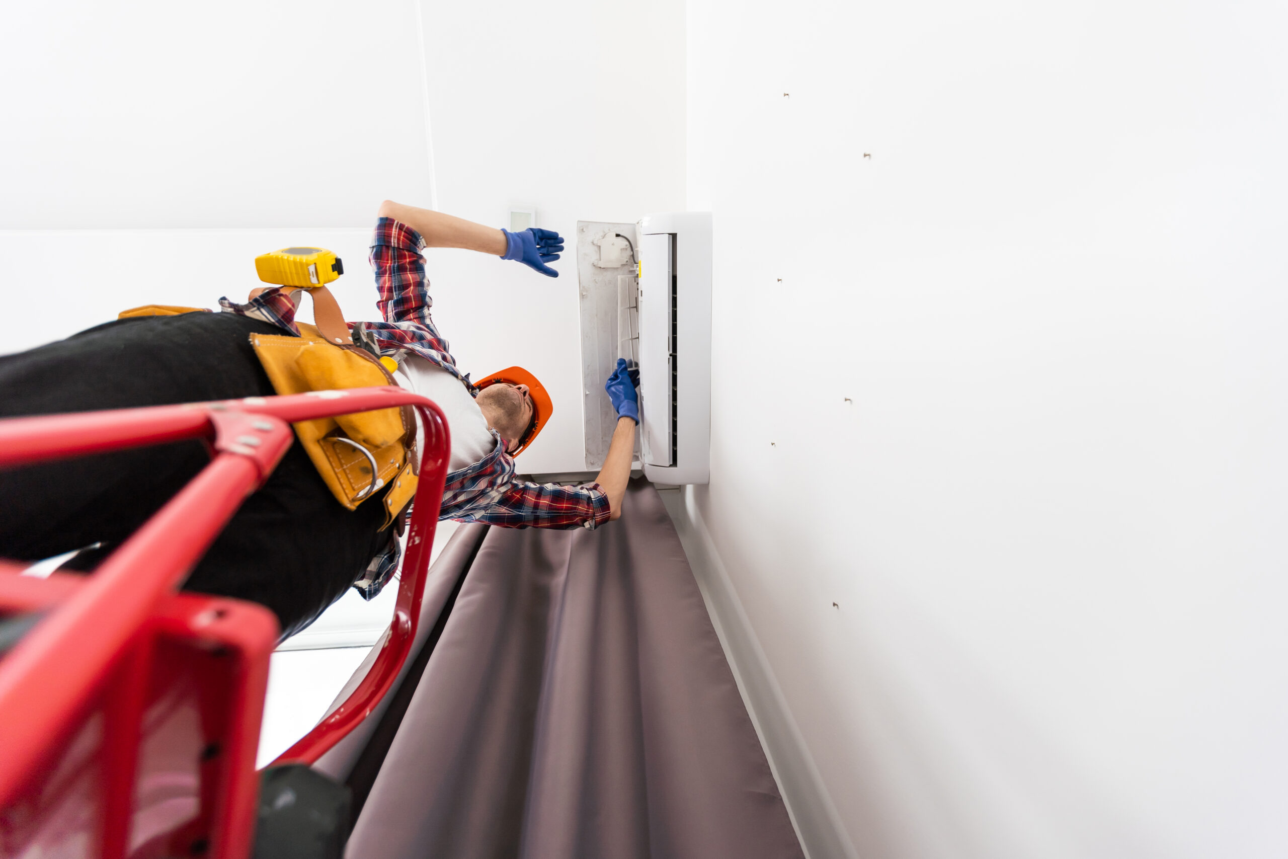 A happy male technician repairing an air conditioner with tools, highlighting the importance of HVAC maintenance and prompting questions like what is the average cost of air duct cleaning