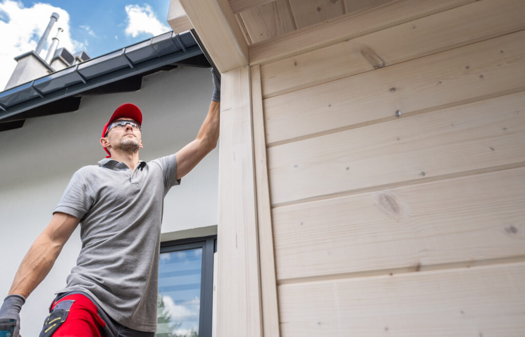 A person performing maintenance on the exterior of a home, possibly assessing the cost of gutter replacement and repairs. 